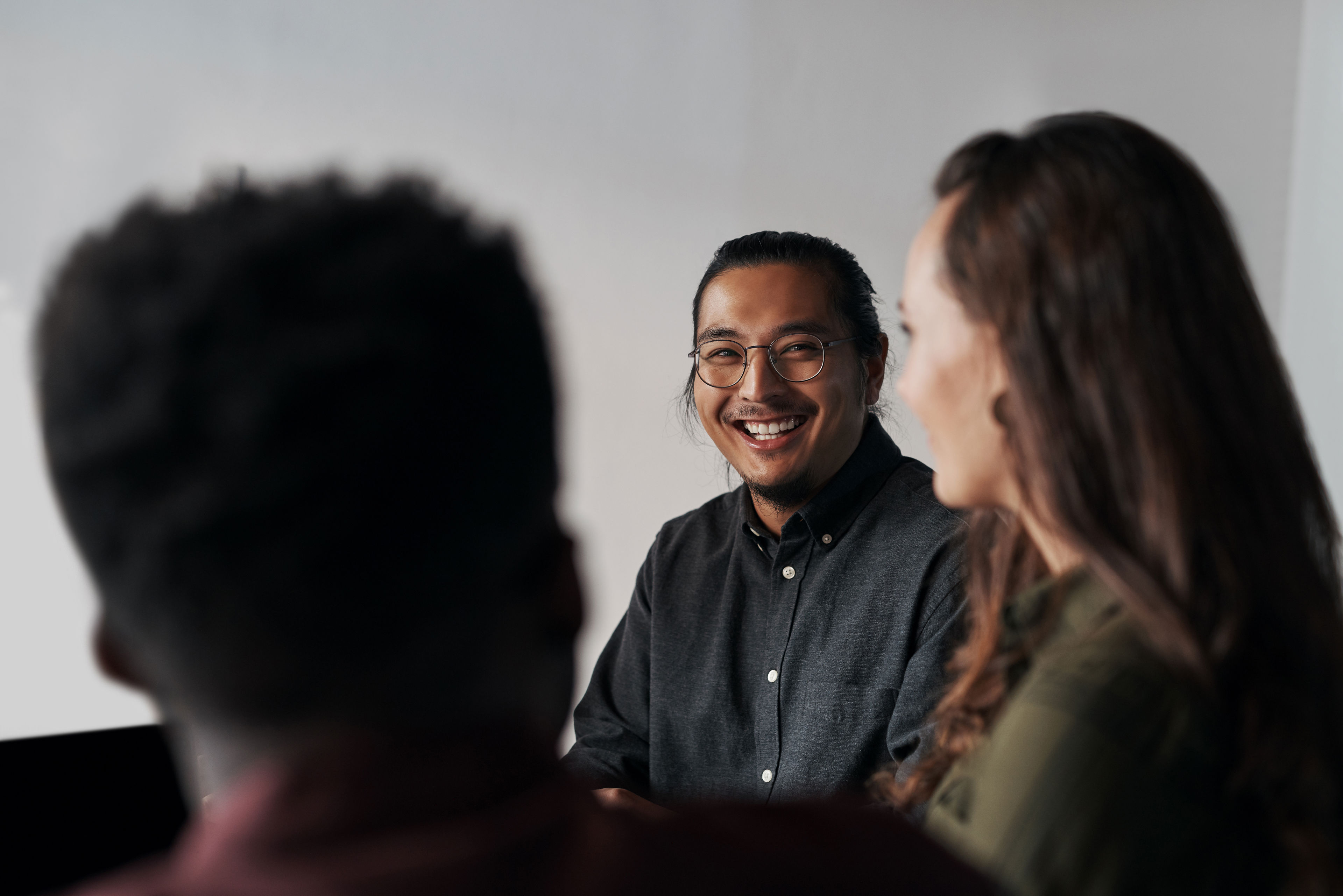 Smilende mand sidder ved siden af en kvinde som kigger på ham. Forgrunden er et baghoved der kigger på dem.